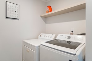 A laundry room with two white washing machines, a shelf with a detergent bottle, and a wall-mounted laundry symbols chart. - 13 mins to Campbell University Boho Retreat (Angier)