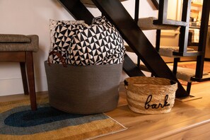 Ein gewebter Korb mit dem Schriftzug 'barl', ein Kissen mit geometrischem Muster und ein Holzstuhl.