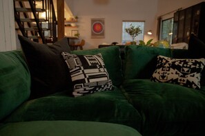 A green sofa with patterned cushions in a room with a staircase and a globe on a table. - Hood Hideaway: Dog-Friendly Mt. Hood Cabin, Private Hot Tub, Sleeps 8 (Rhododendron)