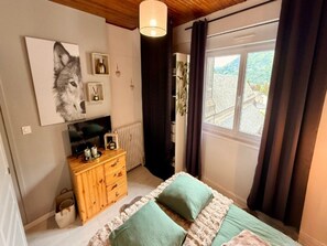 Ein Schlafzimmer mit Bett, Schminktisch, Gemälde, Fenster und Blick ins Freie.