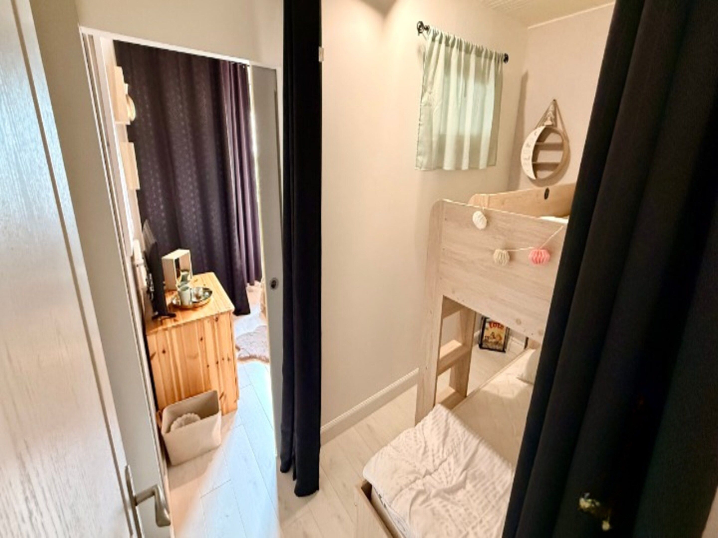 A bedroom with a wooden bunk bed, a bedside table, a mirror, and a curtain.