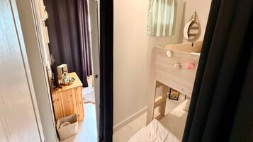 A bedroom with a wooden bunk bed, a bedside table, a mirror, and a curtain.
