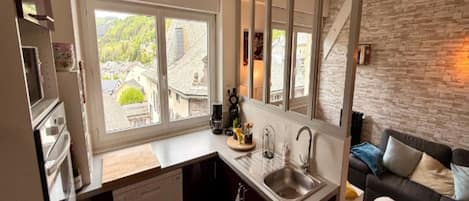 A compact kitchen with a large window, a built-in dishwasher, and a stone wall.