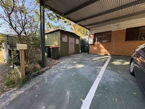 A parking area with a green surface, a car parked on the right, and a small shed with a green door. - Manly Bayside Retreat 3BR 2BA Free Parking (Manly)