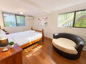 Ein Schlafzimmer mit einem hölzernen Bett, einem schwarzen Ledersessel, einem Nachttisch mit Lampe und einer Wand-Klimaanlage.