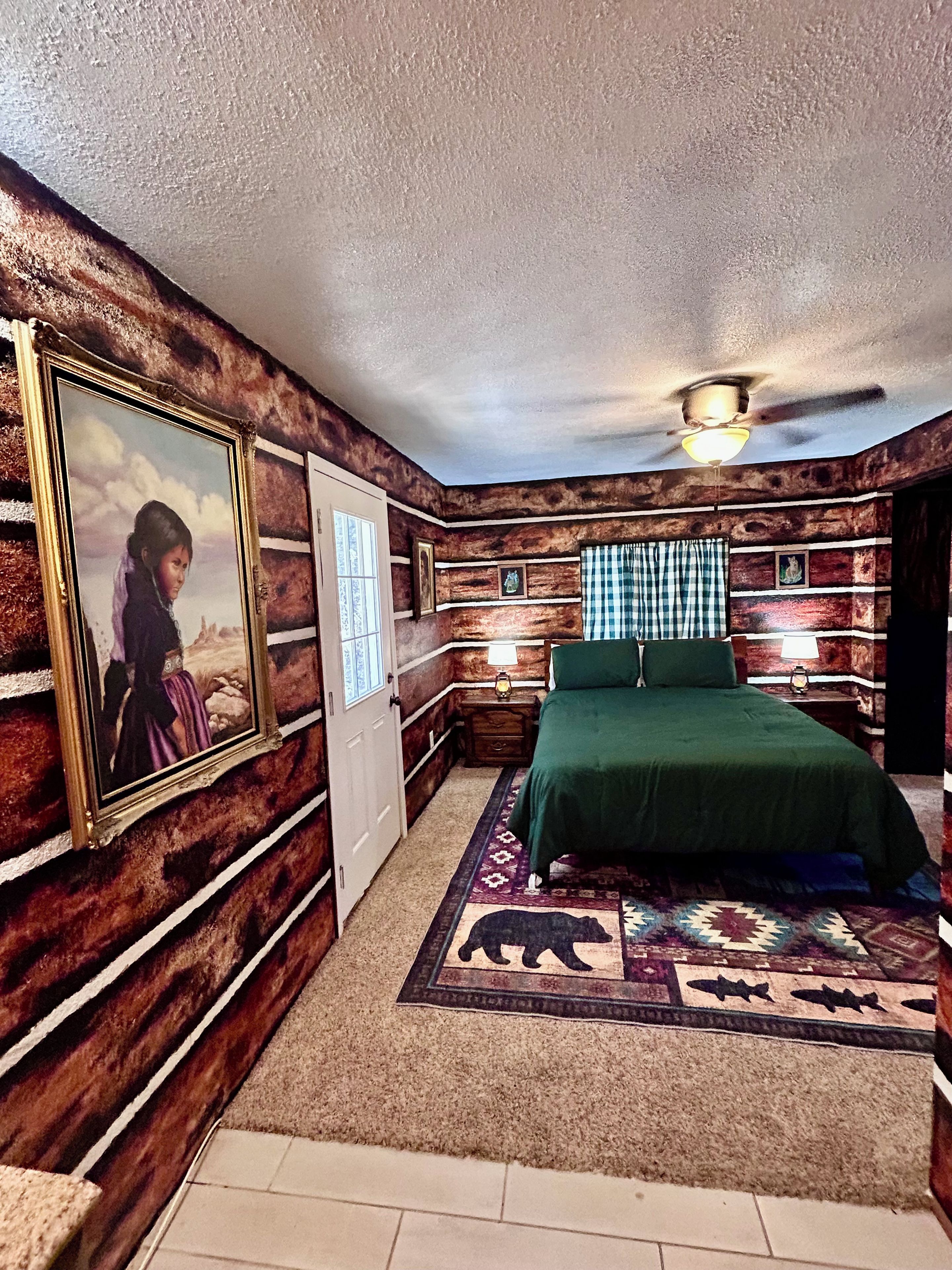 A room with a bed, a ceiling fan, a framed picture on the wall, and a patterned rug.