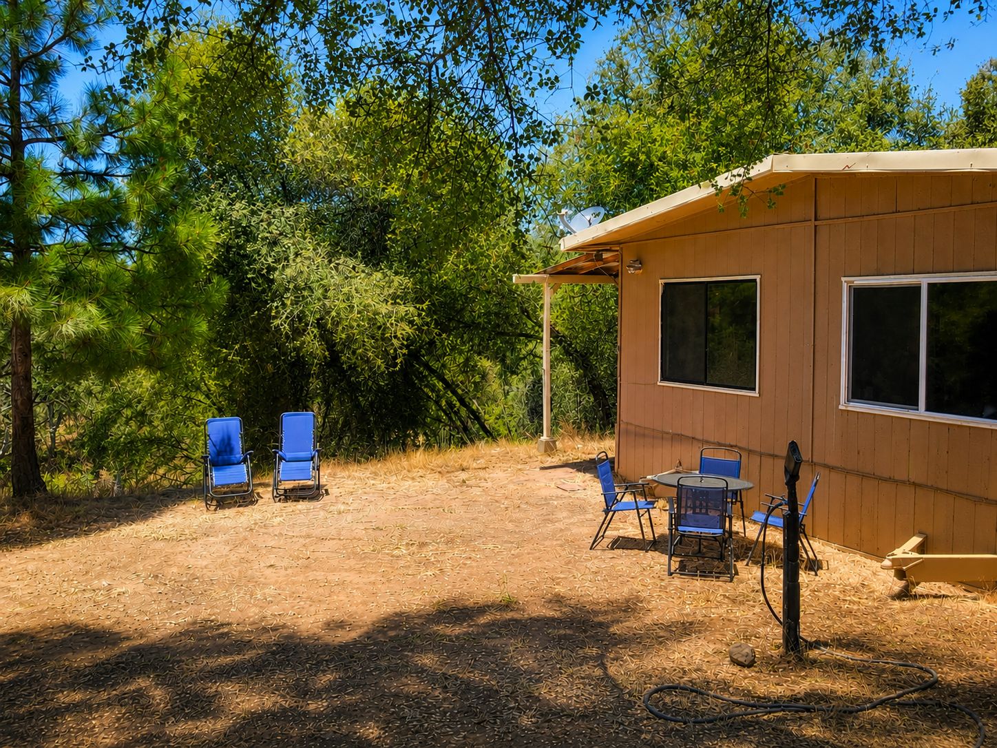 A wooden cabin with a patio area, including two blue chairs and a table.