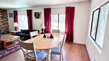 A room with a dining table, chairs, a sofa, a lamp, and a window with curtains.
