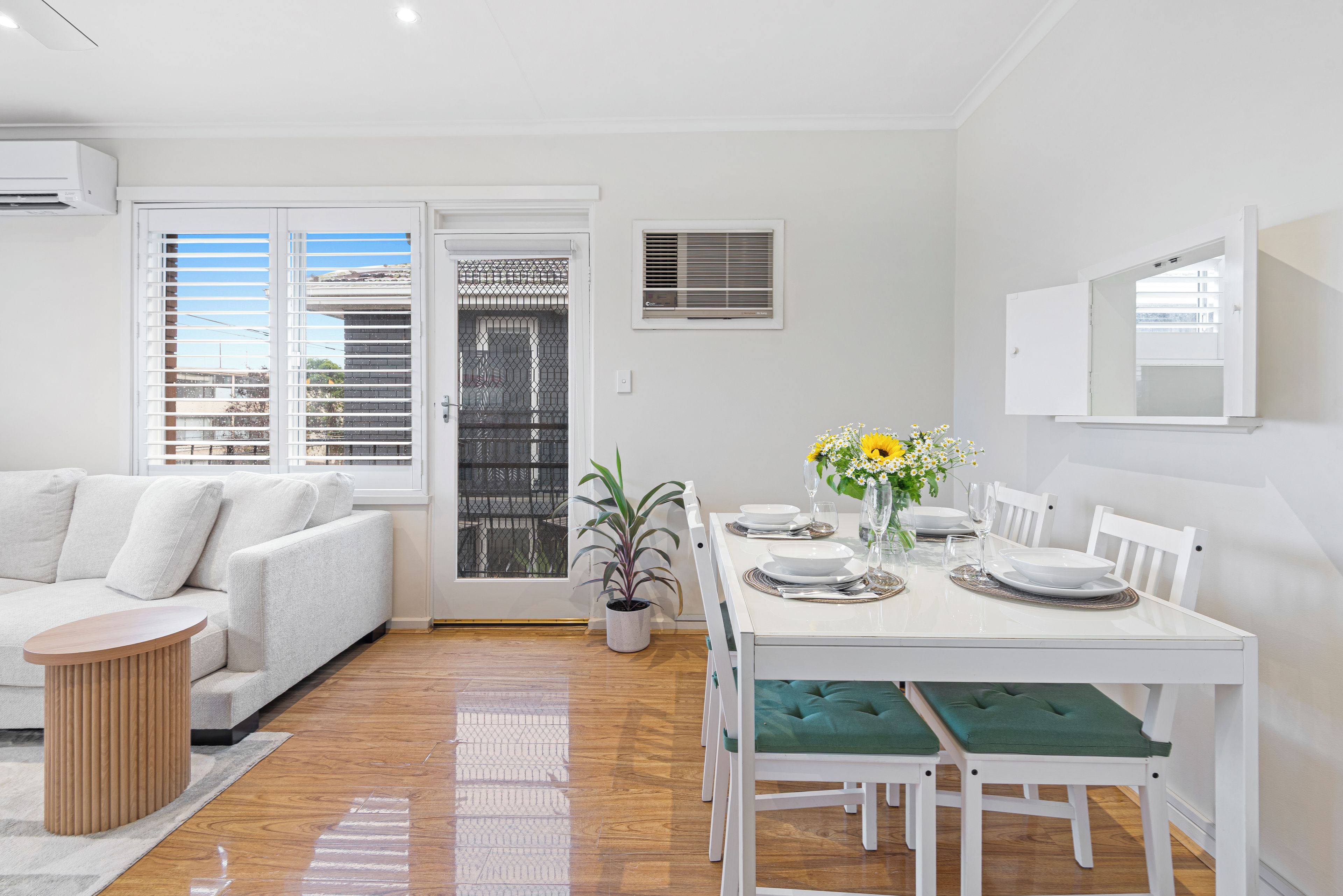 A modern living space with a dining area, white furniture, and a view through a glass door.