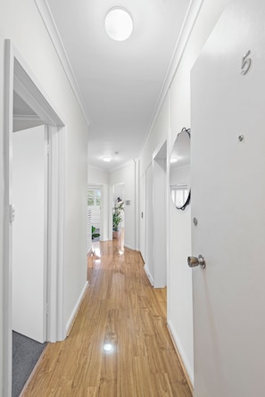 A hallway with white walls and wooden flooring, leading to a room with a door. - Quiet Sunlit Sanctuary, St Kilda | WiFi, Parking (Saint Kilda East)