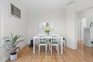 A dining area with a white table, green cushioned chairs, a potted plant, and a wall-mounted picture. - Quiet Sunlit Sanctuary, St Kilda | WiFi, Parking (Saint Kilda East)