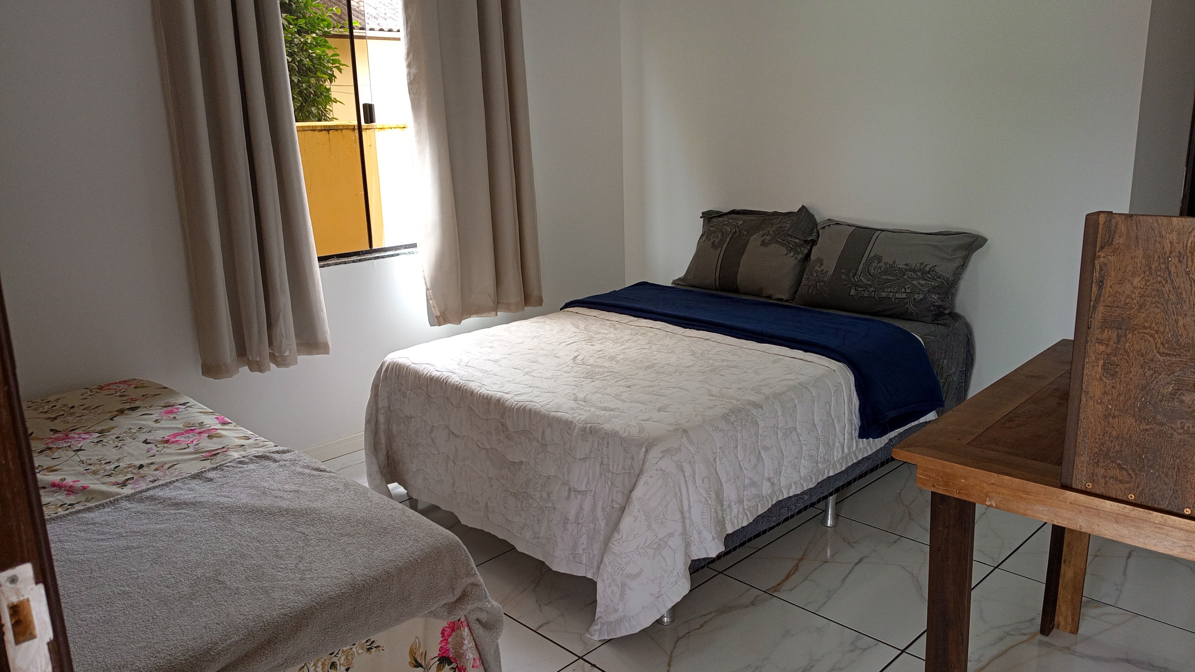 A bedroom with a bed, a wooden table, and a window with curtains.