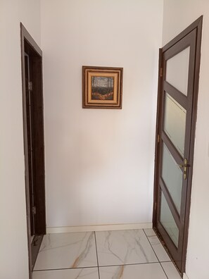 Un pasillo con suelo de baldosas, un cuadro en la pared y dos puertas de madera.