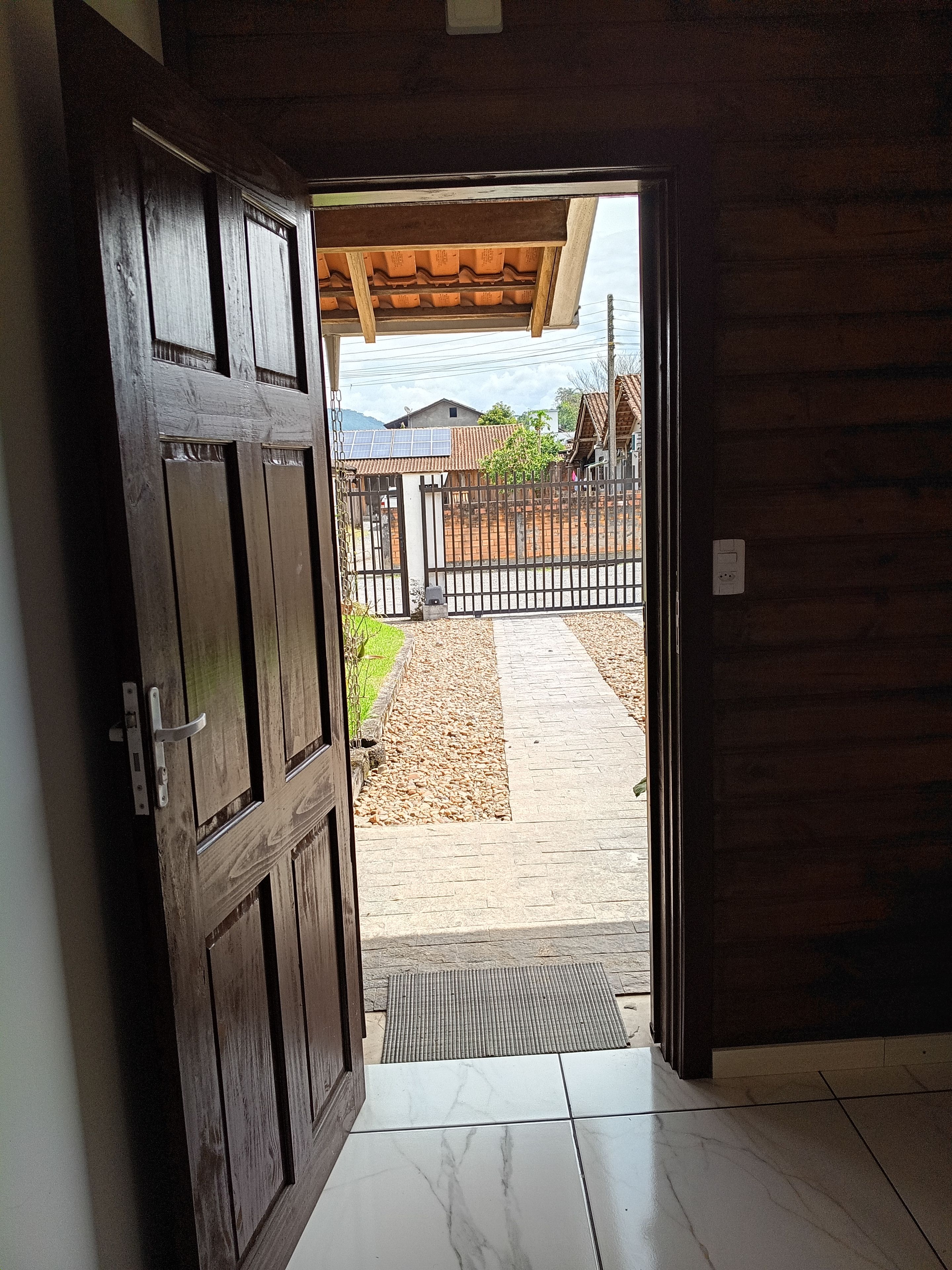 Una porta in legno che dà su un'area esterna con pavimento in piastrelle, un cancello in metallo e vista su una casa con tetto in tegole.