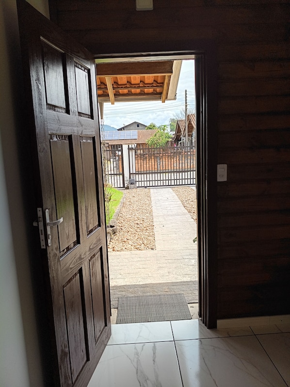A wooden door leading to an outdoor area with a tiled floor, a metal gate, and a view of a house with a tiled roof.