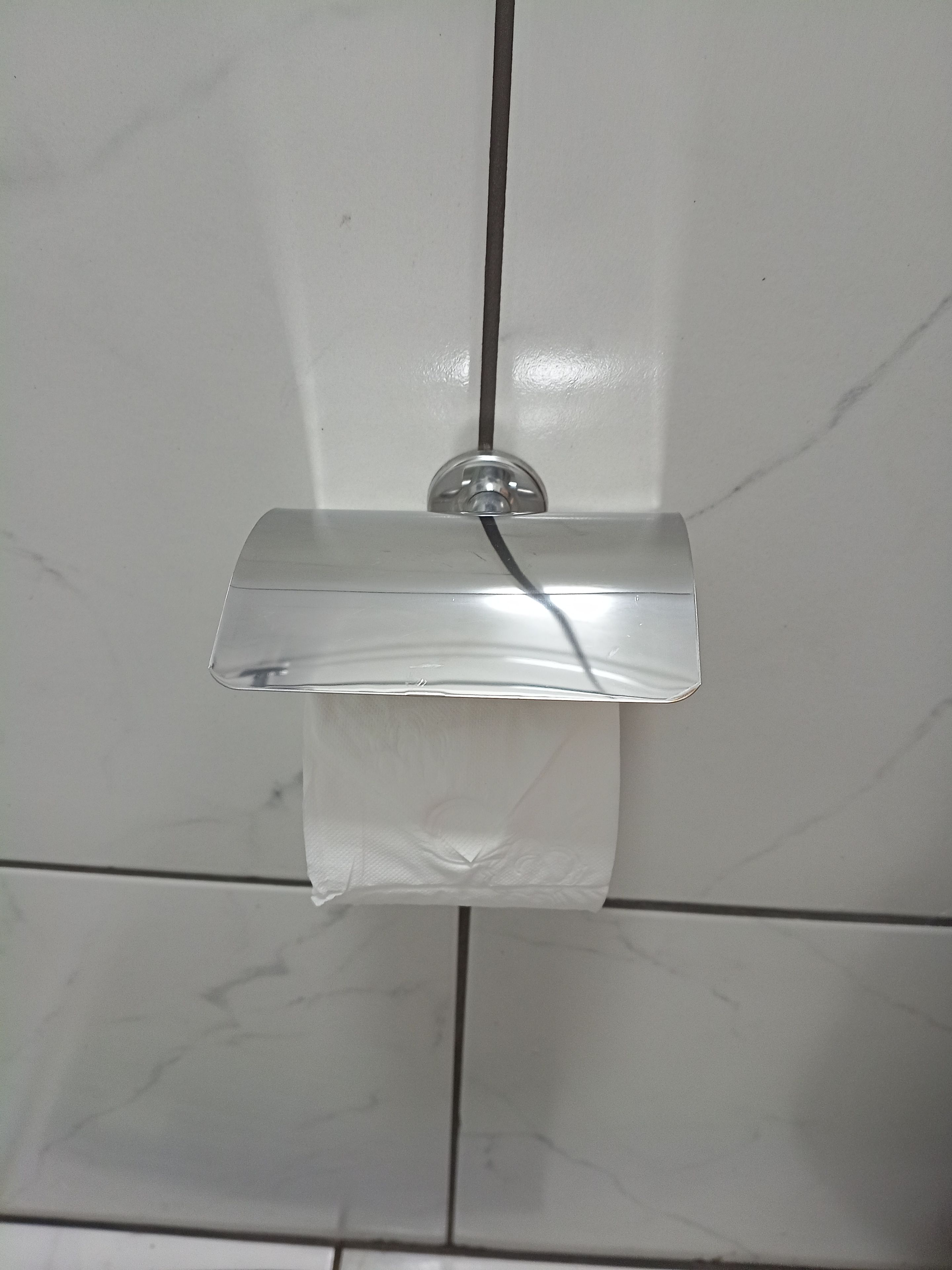 Un bagno con una parete rivestita in piastrelle bianche, un portasapone in vetro trasparente fissato alla parete e un rotolo di carta igienica appeso sotto.
