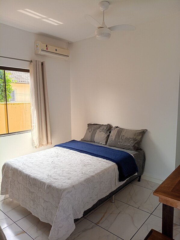 Un dormitorio con cama, ventilador de techo, aire acondicionado, ventana con cortinas y vista al exterior.