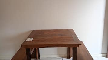 A wooden table with benches in a room with white tiled flooring and a plain wall.