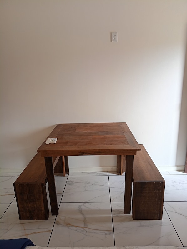 Una mesa de madera con bancos en una habitación con suelo de baldosas blancas y una pared lisa.