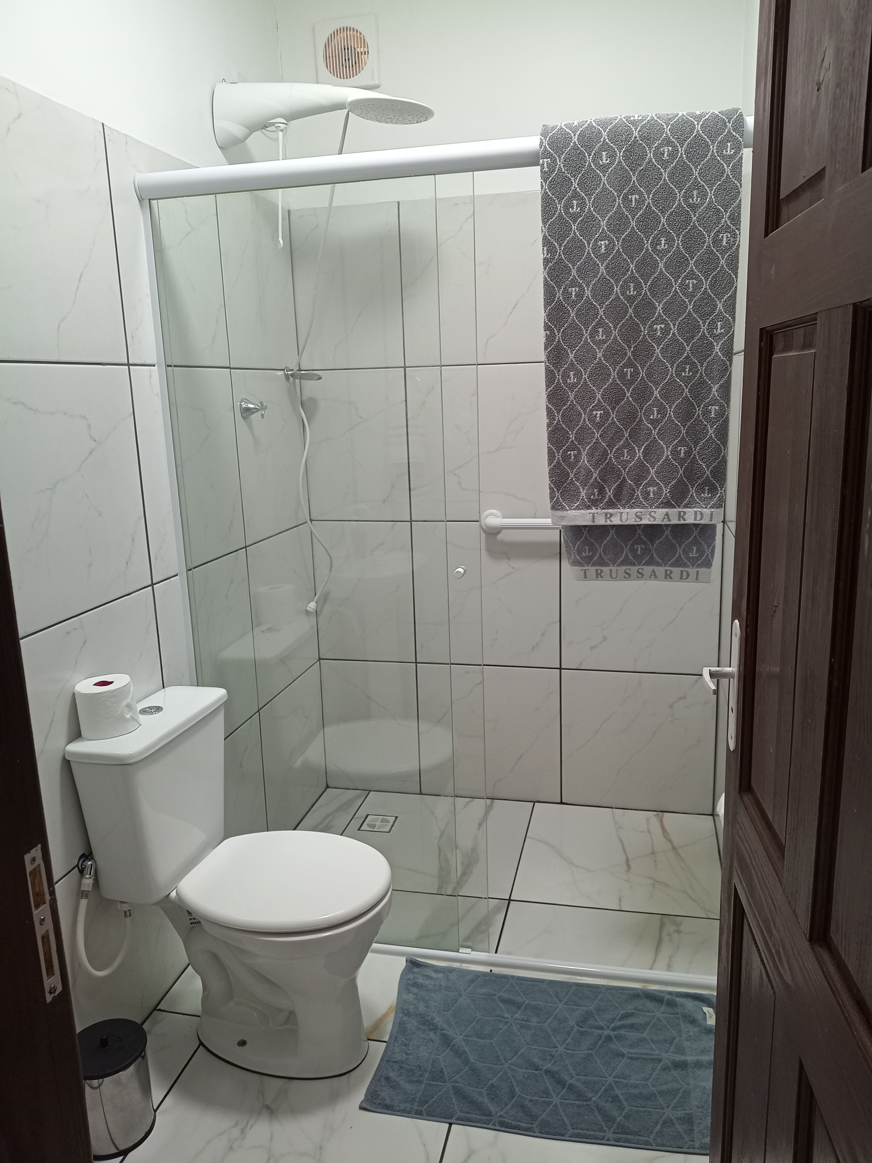 A bathroom with a toilet, shower, and a towel hanging on the wall.