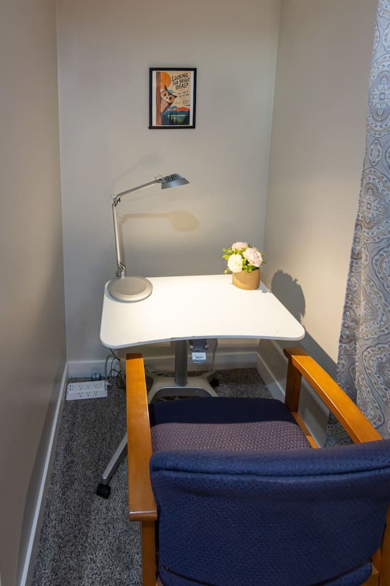 Et hjørnekontor med skrivebord, stol, lampe og et billede i ramme på væggen.