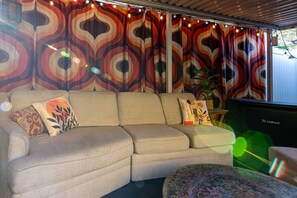 Ein beiges Sofa mit gemusterten Kissen, ein kleiner runder Tisch und ein LifeTrend TV.