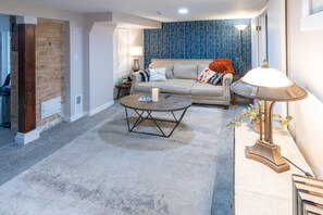 A living room with a sofa, coffee table, lamp, and a brick wall. - Deco Garden Lounge - With Sauna Access! (Ogden)
