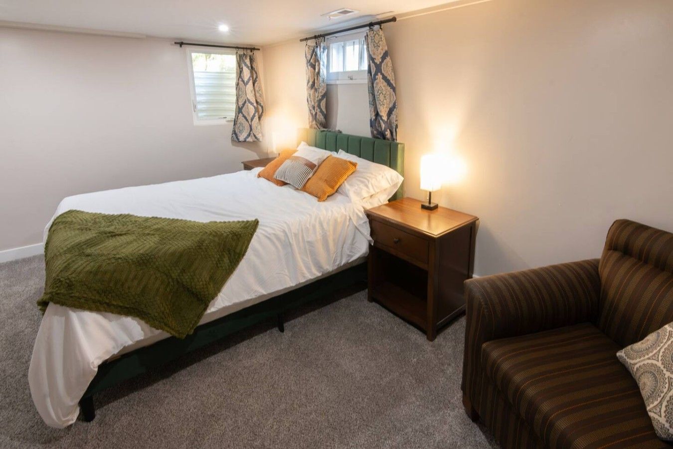 Une chambre à coucher avec un lit, une table de chevet, une lampe et un fauteuil à rayures.