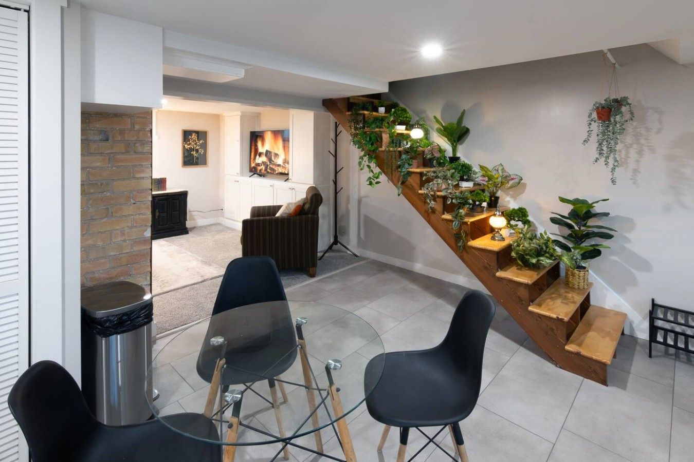 A modern interior with a dining area, a staircase with plants, and a fireplace.