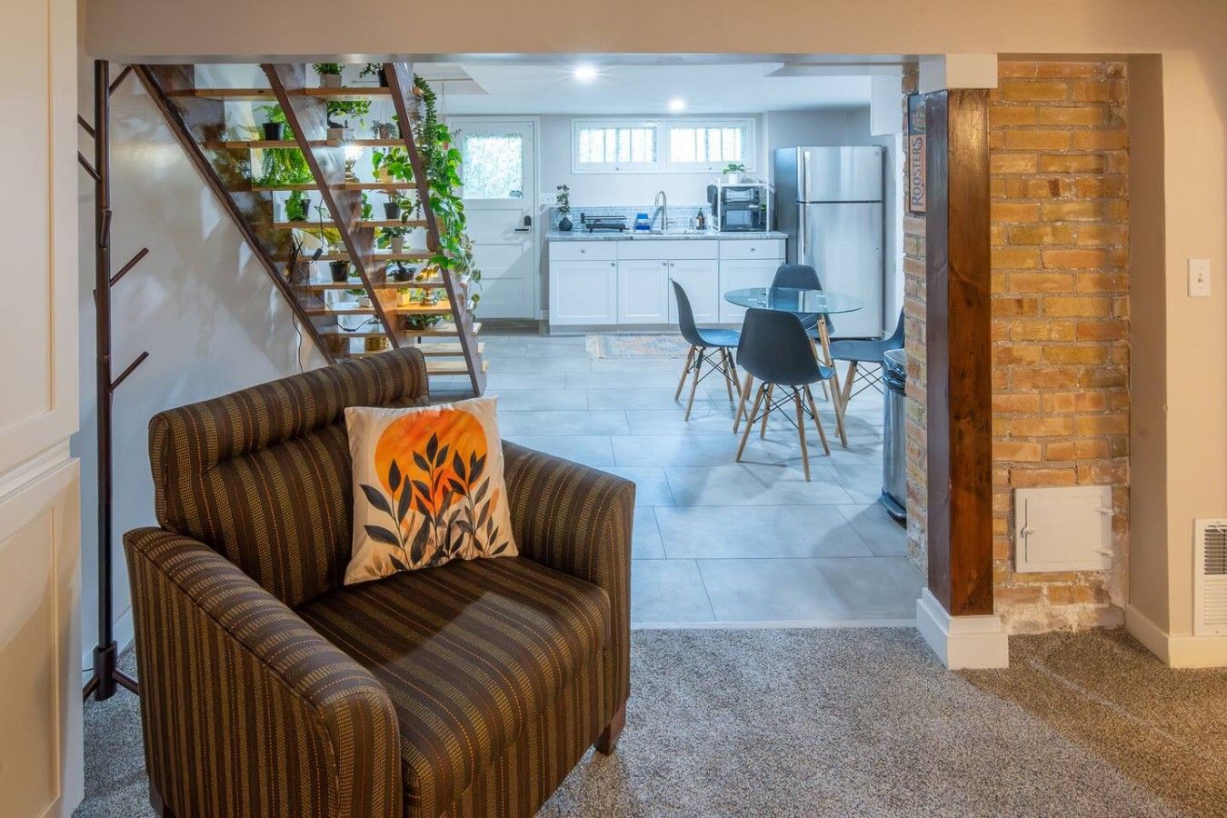 Un salon avec un canapé et une table basse, un escalier agrémenté de plantes, une cuisine avec des meubles blancs et un coin repas avec des chaises.
