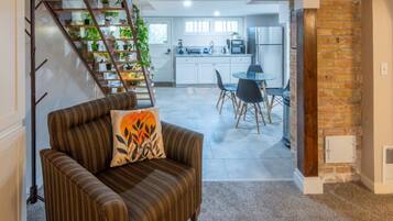 Un salon avec un canapé et une table basse, un escalier agrémenté de plantes, une cuisine avec des meubles blancs et un coin repas avec des chaises.