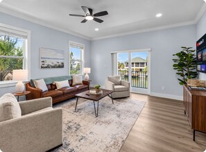 A living room with a brown leather sofa, a beige armchair, a coffee table, and a TV mounted on the wall. - Waterfront Home w/ Pool and Kayaks near Beaches (Hernando Beach)