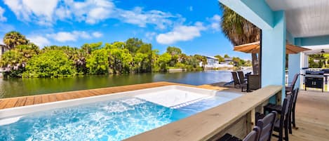 A pool area with a wooden deck, lounge chairs, and a view of a body of water and greenery.
