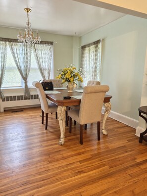 Une salle à manger avec une table en bois, des chaises, un lustre et un vase rempli de fleurs.