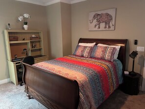 A bedroom with a bed, a desk, a chair, a lamp, and a shelf with decorative items. - The Mcdonough Luxury Island Suite (McDonough)