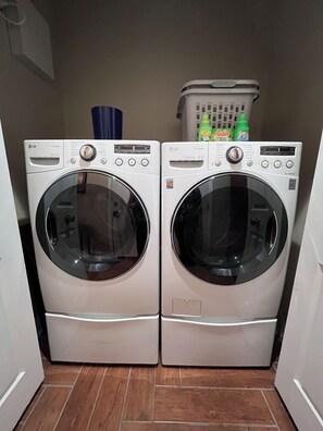 Two front-loading LG washing machines in a laundry room with a basket containing cleaning supplies on top. - The Mcdonough Luxury Island Suite (McDonough)