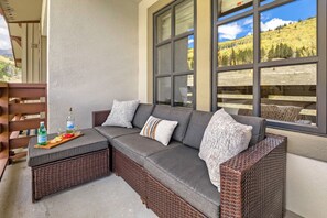 A wicker sectional sofa with cushions, a small table with a bottle and glasses, and a wooden bench. - Penthouse Ski Access, King Bed, Hot Tubs, Views (Copper Mountain)