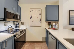 Een moderne keuken met grijze kastjes, een roestvrijstalen fornuis en een betegelde achterwand.