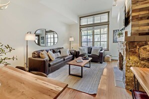 A modern living room with a fireplace, leather sofas, a coffee table, and a large window. - Penthouse Ski Access, King Bed, Hot Tubs, Views (Copper Mountain)