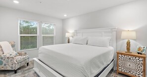 Ein Schlafzimmer mit einem großen Bett, zwei Nachttischen, einem Sessel und einer dekorativen Wandverkleidung.