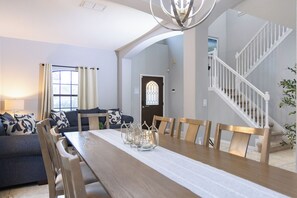 A dining area with a wooden table, chairs, and candle holders. There is a staircase to the right and a door with a stained glass window in the background. - 5-Bedroom Near Disney / Free Pool Heat & Spa / Game Room (Clermont)