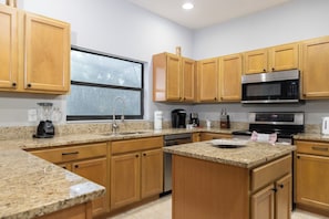A kitchen with granite countertops, wooden cabinets, a stainless steel microwave, and a coffee maker. - 5-Bedroom Near Disney / Free Pool Heat & Spa / Game Room (Clermont)
