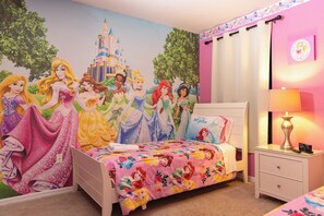 Ein Schlafzimmer mit einem Bett, einem Nachttisch, einer Lampe und einem Wandgemälde mit Disney-Prinzessinen.