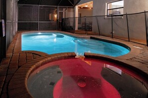 Ein Innenpool mit einem roten Whirlpoolbereich, umgeben von Ziegelböden und einer Glaskonstruktion.