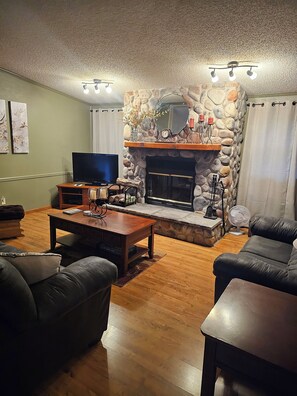 A living room with a stone fireplace, leather sofas, a coffee table, a flat-screen TV, and a stone accent wall. - Enjoyable 3-bedroom house with AC in charming Gwinn (Gwinn)