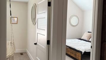 Un couloir menant à une chambre à coucher, où se trouvent un lit, un fauteuil suspendu et une porte dotée d’un miroir.