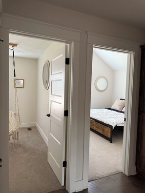 A hallway leading to a bedroom with a bed, a hanging chair, and a door with a mirror.