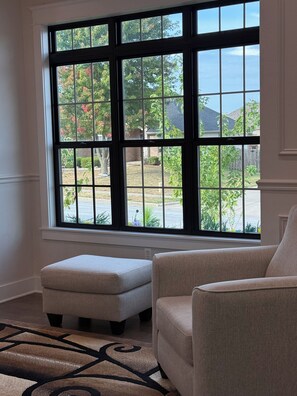 Ein Zimmer mit einem großen Fenster, einem beigen Sessel und dazugehörigem Fußhocker.