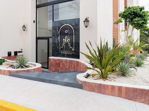 A building entrance with a black marble facade, a logo with a stylized leaf, and a landscaped garden with agave plants. - Vista Vigía Loft · Ideal for 2 in Mazatlan (Mazatlán)