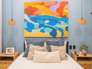 A bedroom with a bed, two nightstands, a wall-mounted abstract painting, and two hanging wicker lamps. - Vista Vigía Loft · Ideal for 2 in Mazatlan (Mazatlán)
